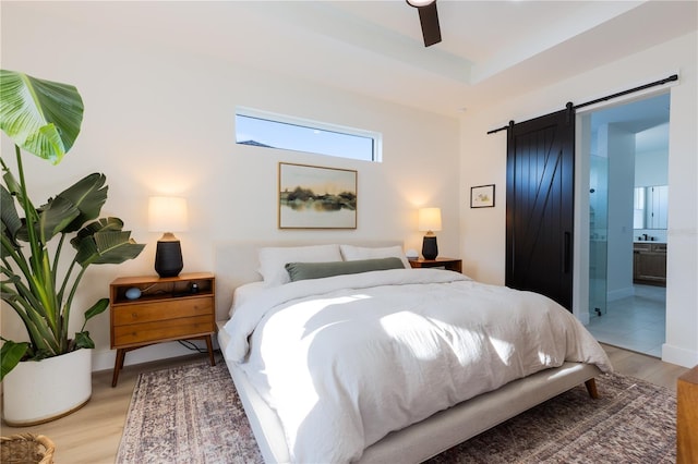 bedroom with light hardwood / wood-style floors, a barn door, ceiling fan, and ensuite bathroom