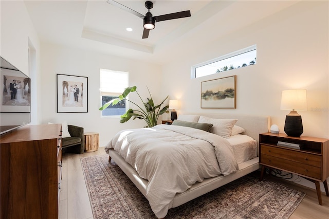 bedroom featuring a raised ceiling, ceiling fan, and light wood-type flooring