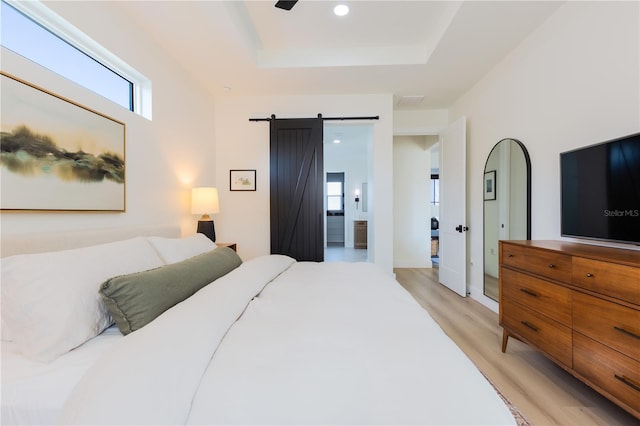 bedroom with a tray ceiling, light hardwood / wood-style floors, and a barn door