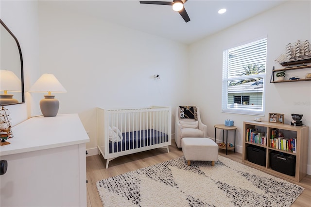 bedroom with ceiling fan, a nursery area, and light wood-type flooring