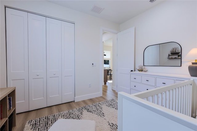 bedroom with a nursery area, a closet, and light wood-type flooring