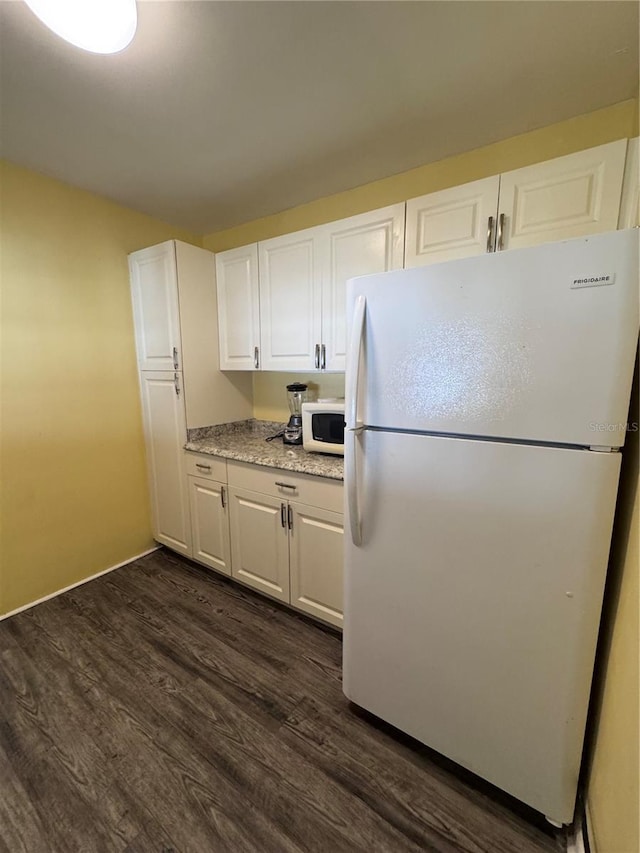 kitchen featuring white appliances, dark wood-type flooring, light stone countertops, and white cabinets