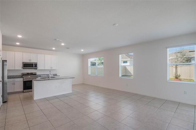 kitchen with sink, white cabinetry, stainless steel appliances, a center island with sink, and dark stone counters