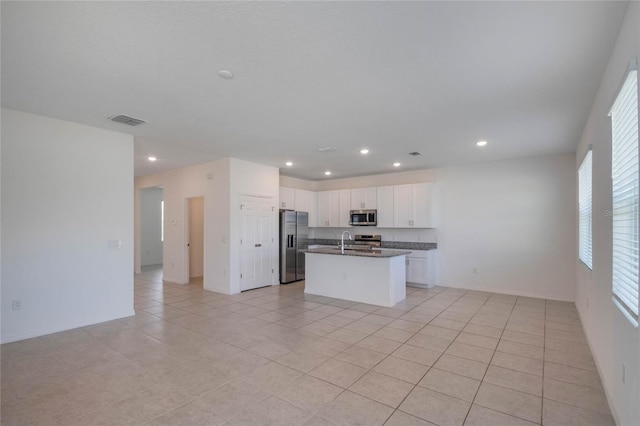 kitchen featuring sink, white cabinets, light tile patterned floors, stainless steel appliances, and a center island with sink