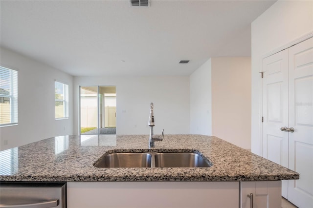 kitchen featuring a kitchen island with sink, sink, white cabinets, and stone countertops