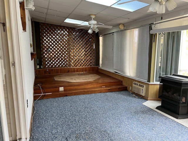 interior space featuring a drop ceiling, light carpet, ceiling fan, and a wood stove