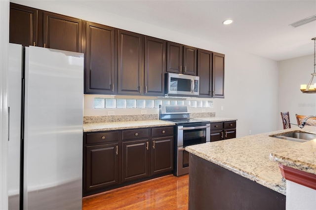 kitchen with sink, decorative light fixtures, dark brown cabinets, stainless steel appliances, and light hardwood / wood-style floors