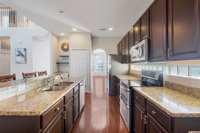 kitchen with a breakfast bar, sink, stainless steel appliances, dark wood-type flooring, and a center island with sink