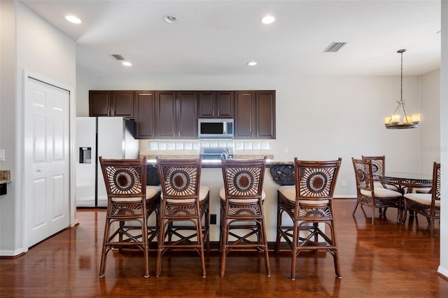 kitchen featuring refrigerator with ice dispenser, decorative light fixtures, dark brown cabinets, and a kitchen bar