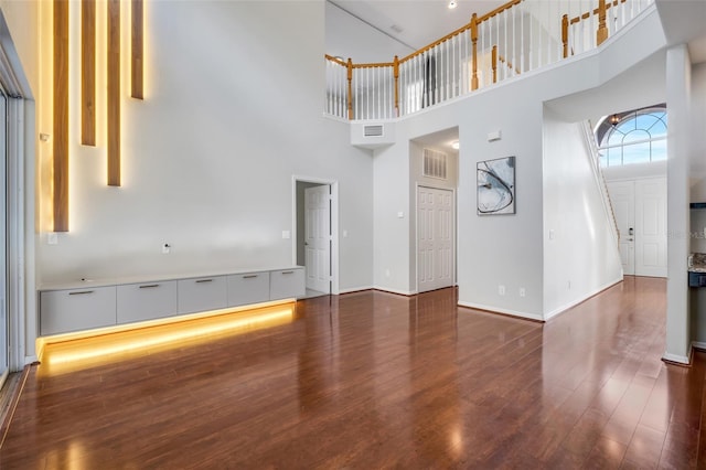 unfurnished living room featuring a towering ceiling and dark hardwood / wood-style flooring