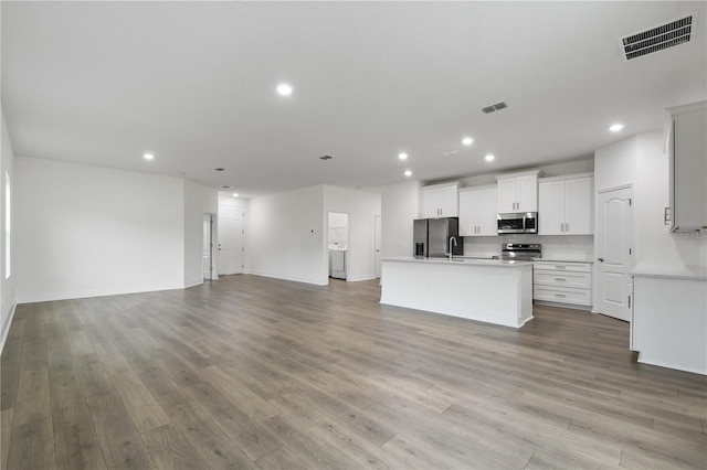 kitchen featuring appliances with stainless steel finishes, washer / dryer, white cabinets, a center island with sink, and light hardwood / wood-style flooring