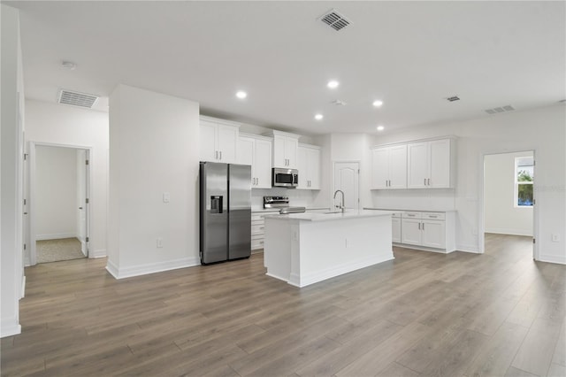 kitchen with sink, stainless steel appliances, light hardwood / wood-style floors, white cabinets, and a center island with sink