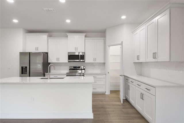 kitchen with sink, appliances with stainless steel finishes, an island with sink, hardwood / wood-style floors, and white cabinets