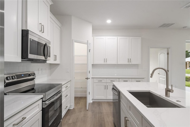 kitchen featuring sink, white cabinetry, stainless steel appliances, light stone counters, and decorative backsplash