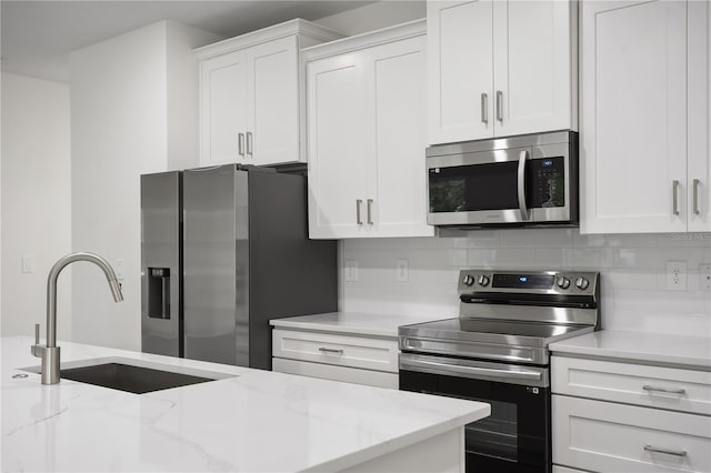 kitchen featuring appliances with stainless steel finishes, sink, white cabinets, decorative backsplash, and light stone countertops