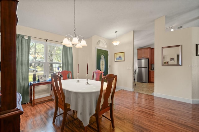 dining space featuring vaulted ceiling, a textured ceiling, a notable chandelier, and light wood-type flooring