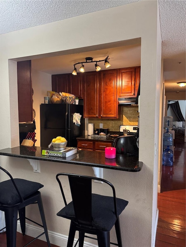 kitchen with stainless steel stove, a breakfast bar, black refrigerator, kitchen peninsula, and dark stone counters