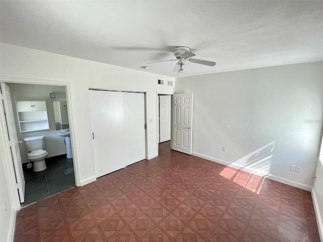 unfurnished bedroom with ceiling fan, ensuite bath, and a textured ceiling