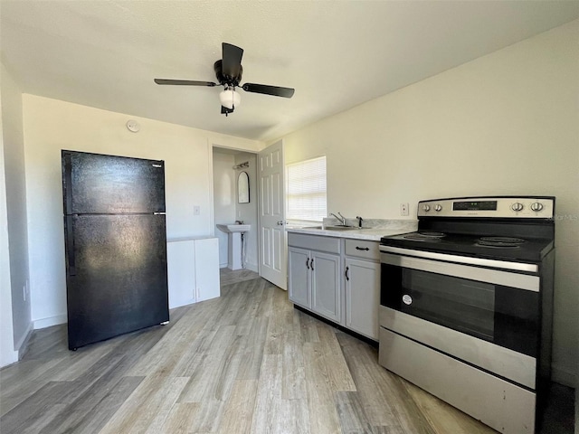 kitchen with sink, white cabinetry, light wood-type flooring, black refrigerator, and stainless steel electric stove