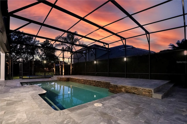 pool at dusk featuring a patio and a lanai