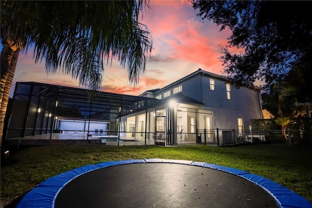 back house at dusk with a yard and glass enclosure