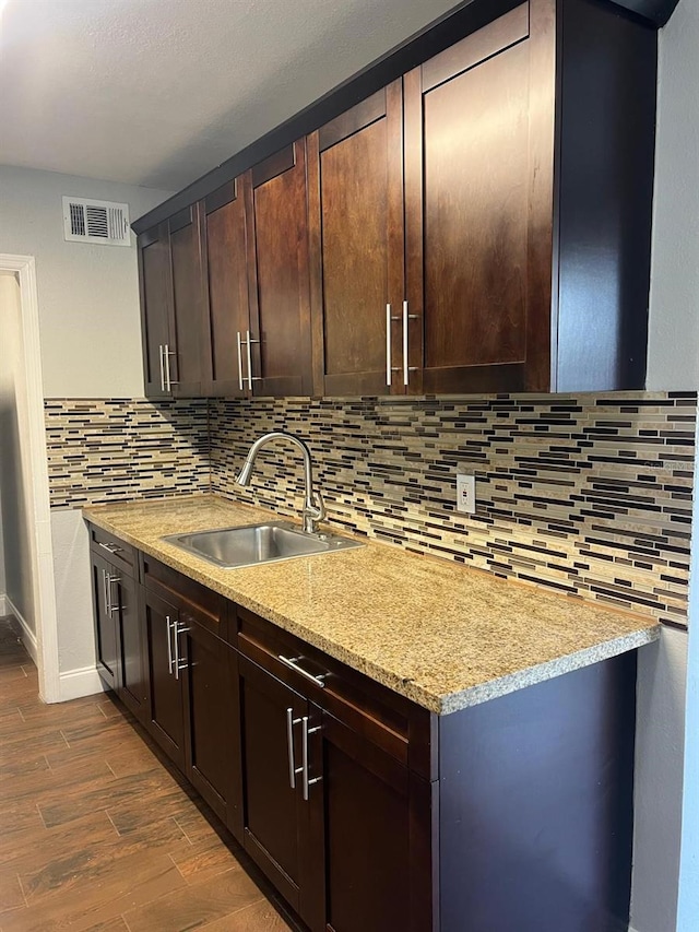 1315 Carlsbad Pl, Orlando, FL 32808 - kitchen with sink, dark wood-type flooring, light stone counters, dark brown cabinetry, and decorative backsplash