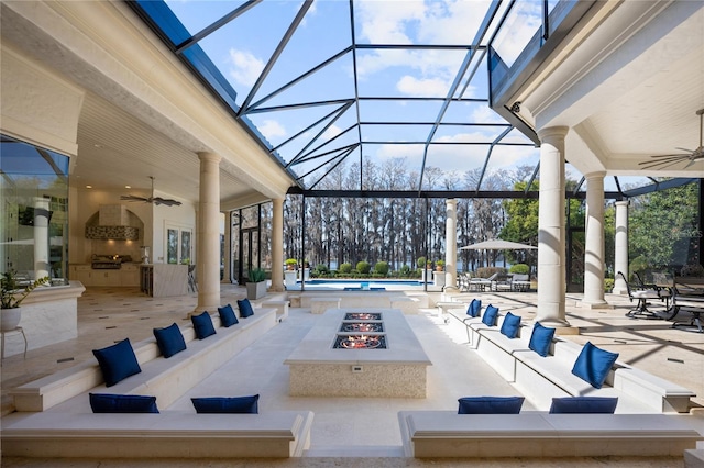 view of patio / terrace featuring a lanai, exterior kitchen, ceiling fan, and an outdoor fire pit