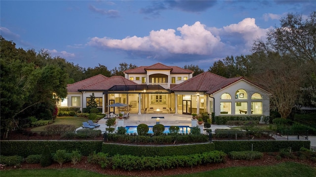 back house at dusk featuring a balcony, a fenced in pool, and a patio area