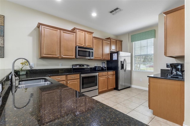 1494 Moon Valley Dr, Davenport, FL 33896 - kitchen with appliances with stainless steel finishes, light tile patterned floors, dark stone countertops, brown cabinetry, and recessed lighting