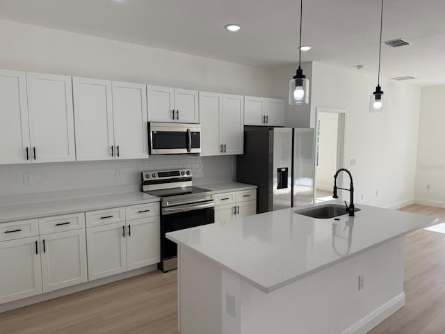 kitchen with a center island with sink, pendant lighting, stainless steel appliances, light stone countertops, and white cabinets