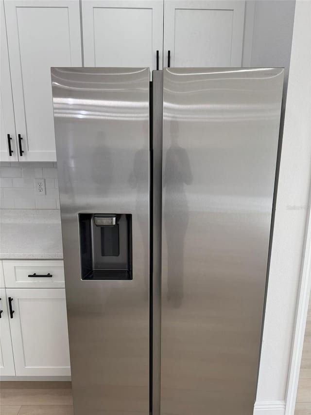 details featuring tasteful backsplash, stainless steel refrigerator with ice dispenser, white cabinets, and light hardwood / wood-style flooring