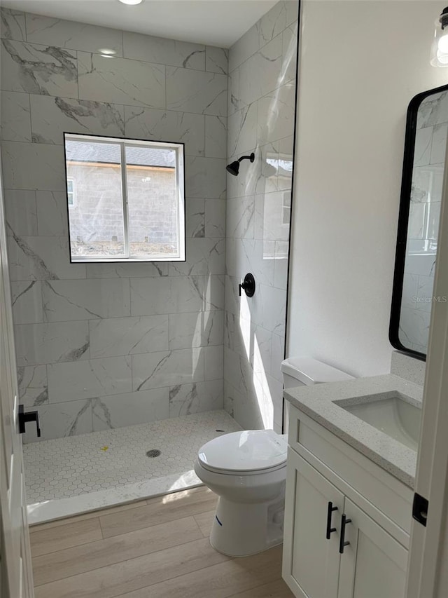 bathroom with vanity, hardwood / wood-style floors, toilet, and tiled shower