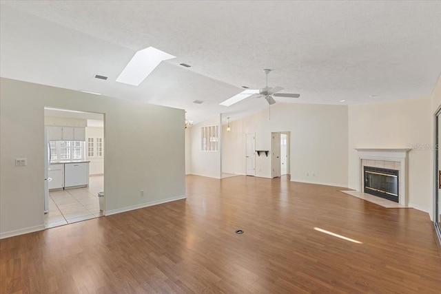 unfurnished living room featuring a tiled fireplace, lofted ceiling with skylight, a textured ceiling, and light wood-type flooring