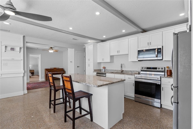 kitchen featuring a kitchen bar, white cabinetry, a center island, a textured ceiling, and appliances with stainless steel finishes