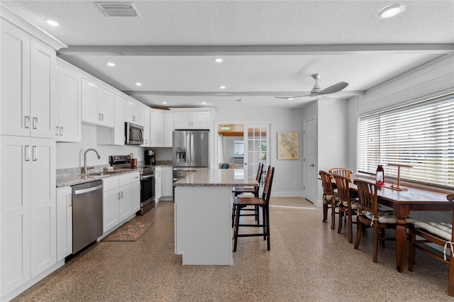 kitchen featuring stainless steel appliances, white cabinetry, a kitchen island, and sink