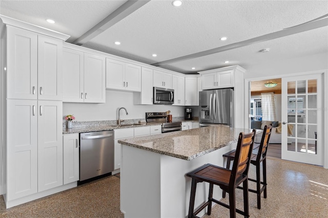 kitchen with a breakfast bar, sink, white cabinetry, light stone counters, and stainless steel appliances