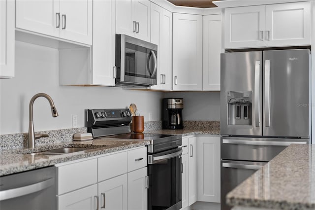 kitchen with light stone countertops, stainless steel appliances, sink, and white cabinets