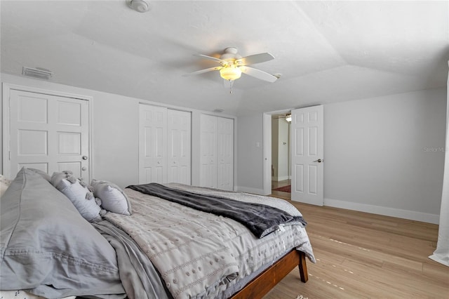 bedroom featuring multiple closets, vaulted ceiling, ceiling fan, and light hardwood / wood-style floors