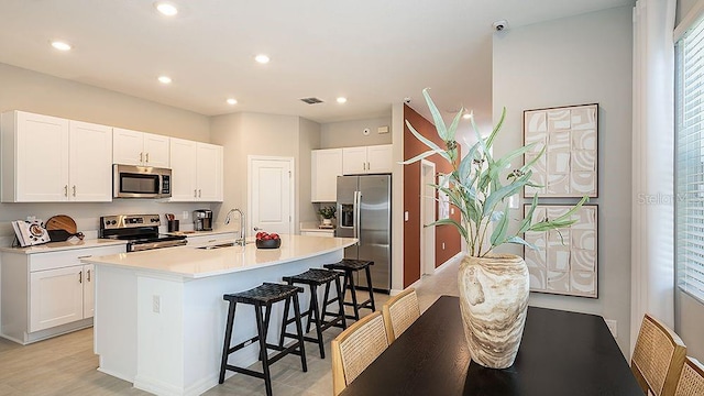 kitchen with a center island with sink, a breakfast bar, white cabinets, and appliances with stainless steel finishes