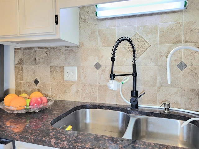 interior details featuring white cabinetry, sink, decorative backsplash, and dark stone counters