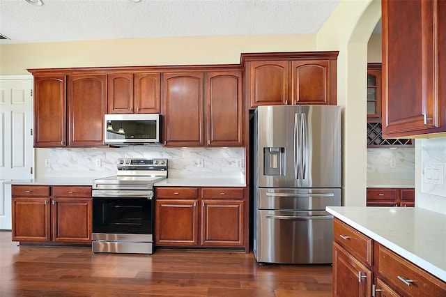 kitchen featuring a textured ceiling, dark hardwood / wood-style flooring, stainless steel appliances, light stone countertops, and backsplash