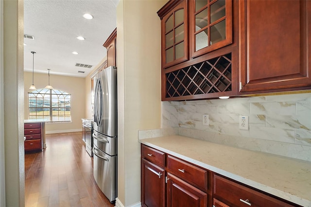 kitchen featuring stainless steel refrigerator, dark hardwood / wood-style floors, tasteful backsplash, a textured ceiling, and decorative light fixtures