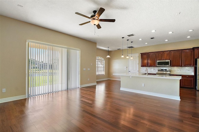 kitchen featuring pendant lighting, dark wood-type flooring, ceiling fan, appliances with stainless steel finishes, and a center island with sink