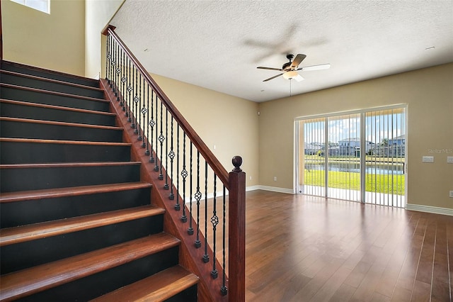 stairs with a water view, ceiling fan, a textured ceiling, and hardwood / wood-style flooring