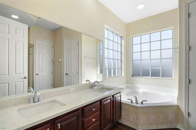 bathroom featuring a relaxing tiled tub and vanity