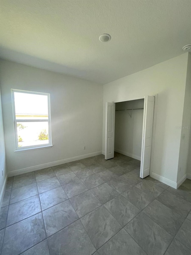 unfurnished bedroom with a textured ceiling, baseboards, and a closet