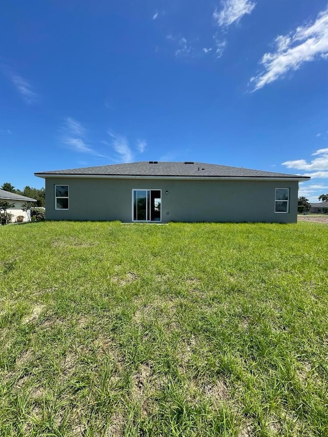 rear view of property featuring a lawn and stucco siding