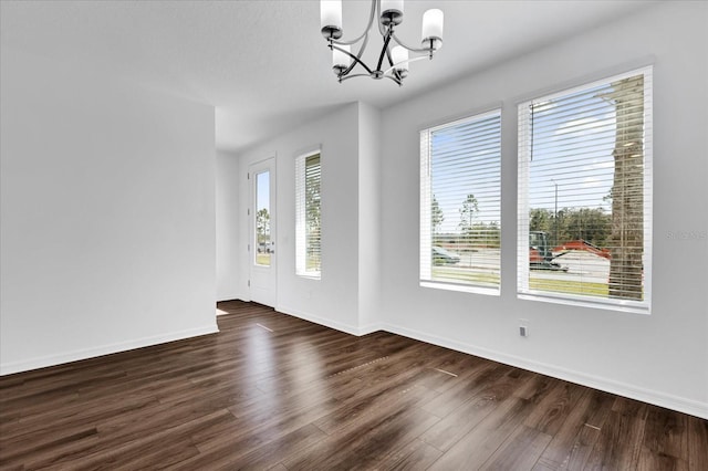 empty room with dark wood-type flooring and a chandelier