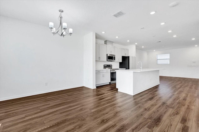 kitchen with white cabinetry, hanging light fixtures, appliances with stainless steel finishes, dark hardwood / wood-style floors, and a kitchen island with sink