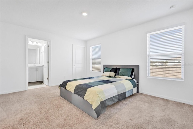 bedroom with ensuite bath, baseboards, and light colored carpet